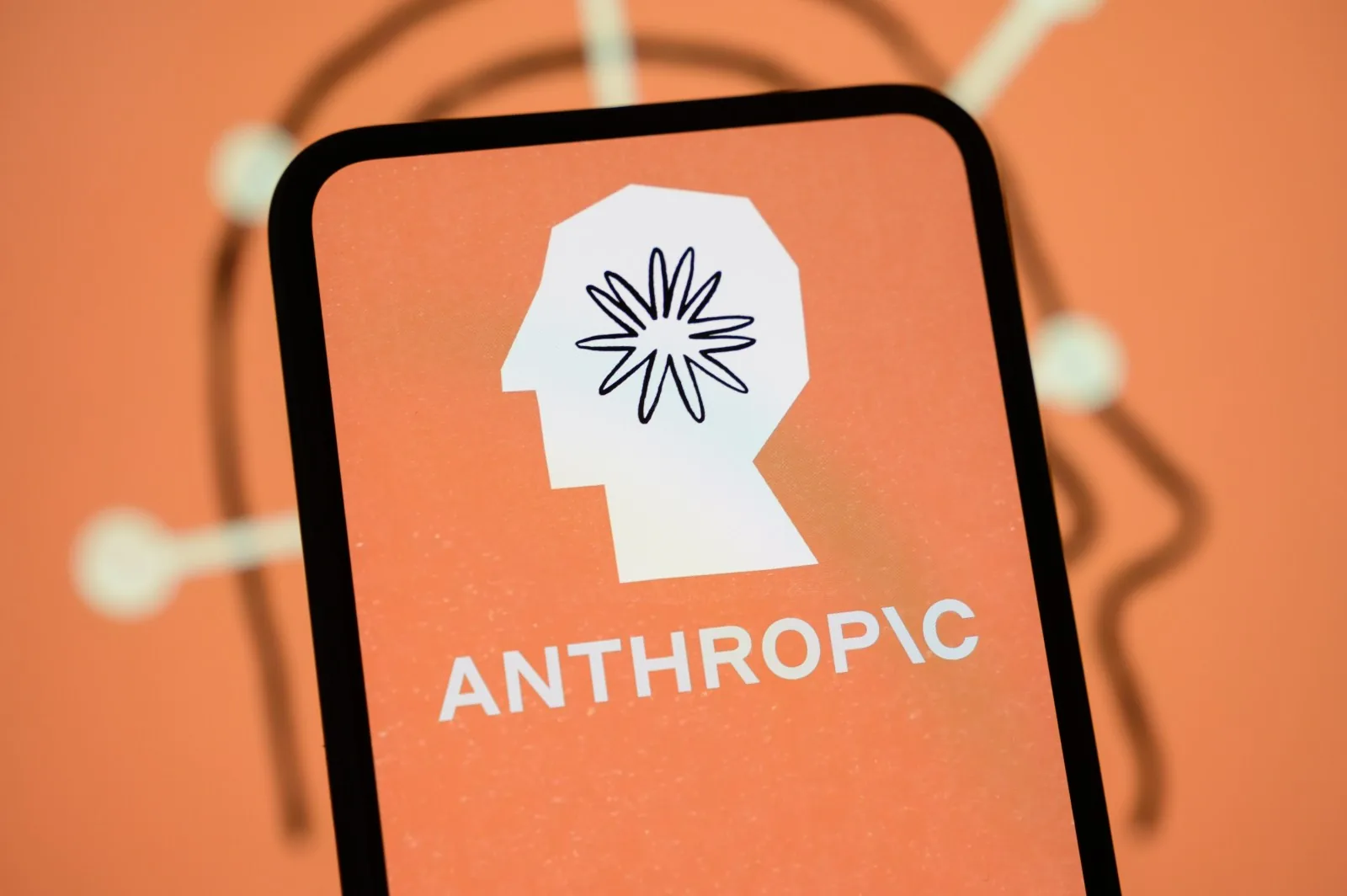 The Anthropic logo on a phone screen against an orange background
