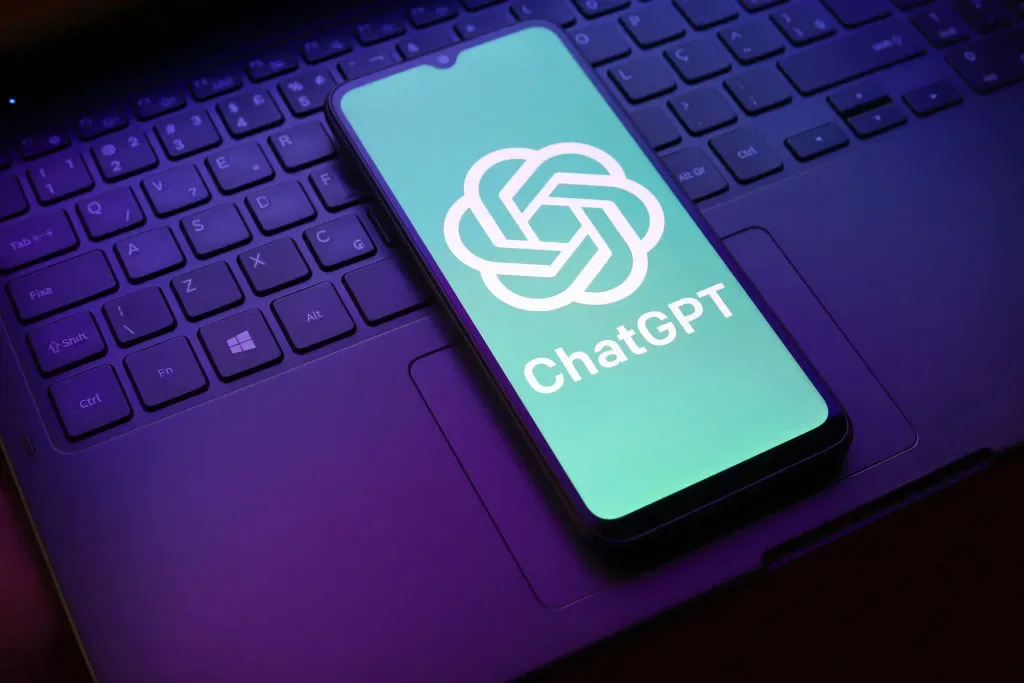 A phone on a laptop keyboard with the ChatGPT logo on the screen